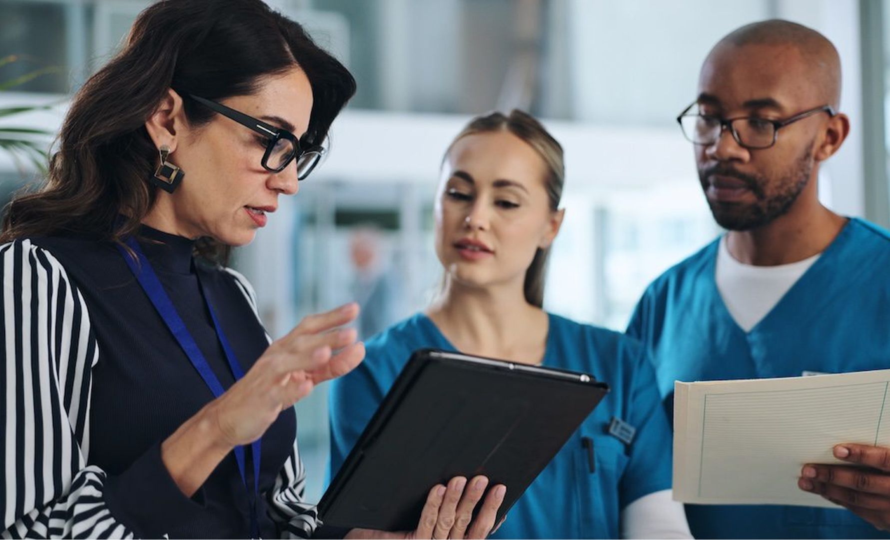 Three professionals in a care environment discussing information on a digital tablet and document.
