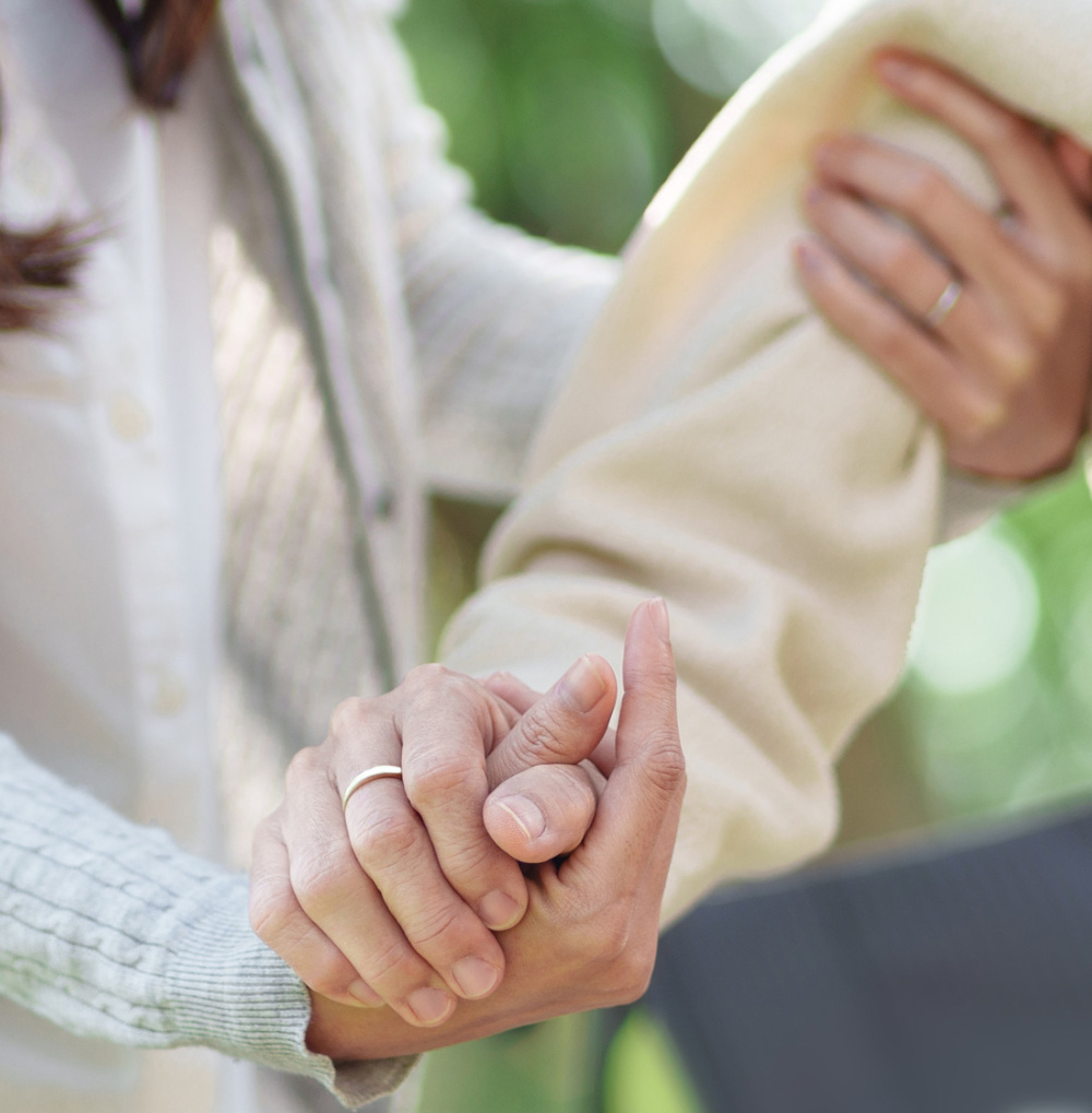 Two people holding hands with one person supporting the other by the shoulder in a caring gesture.