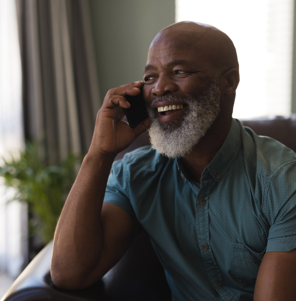 Senior man smiling and talking on a smartphone while seated indoors in a comfortable living space.