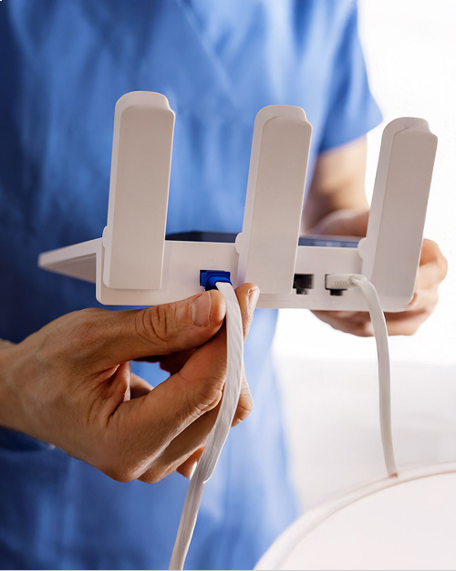 Person connecting an Ethernet cable to a white wireless router with three antennae.