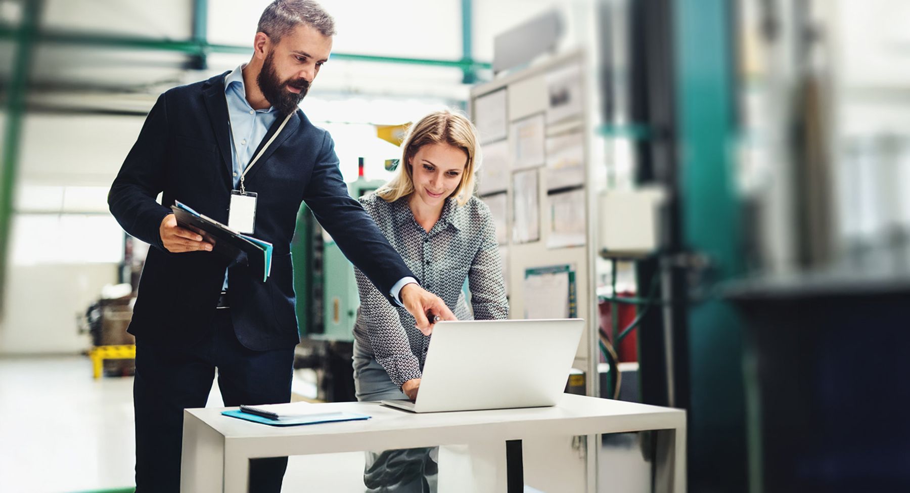 Two professionals collaborating over a laptop in an industrial office workspace.