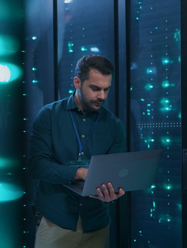 Man using laptop in a server room with illuminated networking equipment