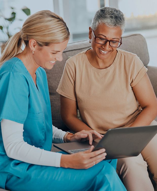 Two adults sitting on a couch engaged in a discussion while looking at a laptop screen together in a senior living care environment.