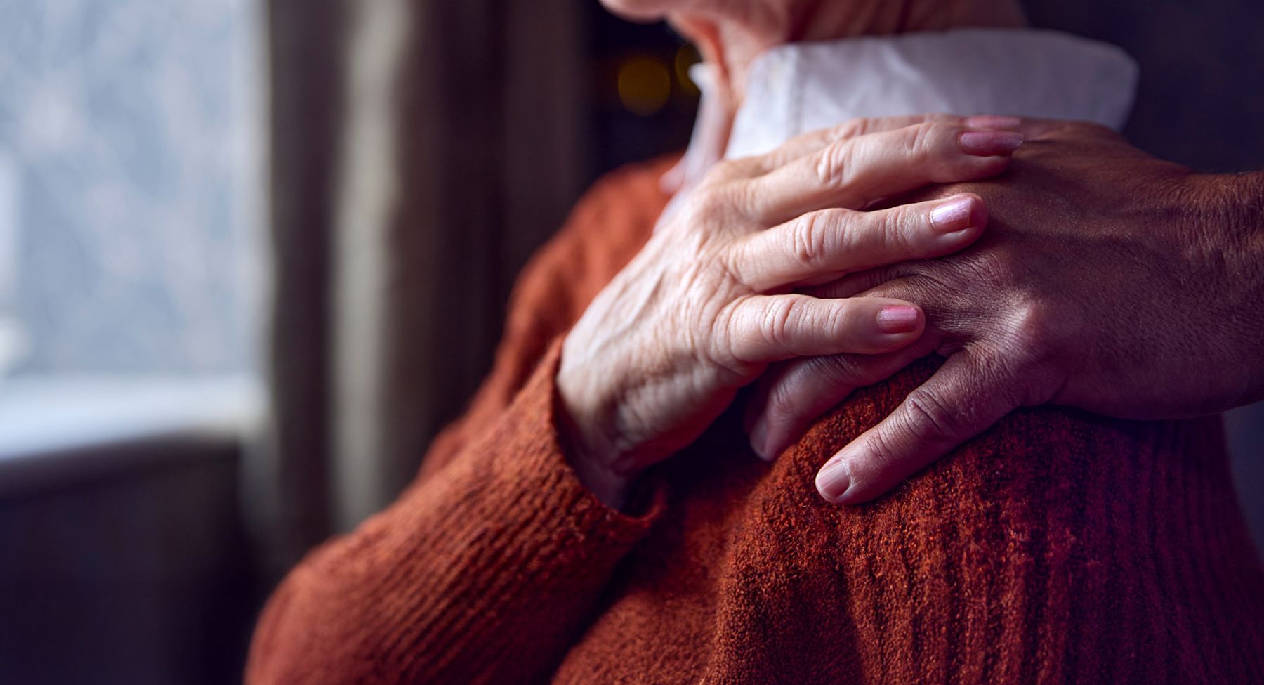 Two hands gently holding each other indoors, symbolizing support in a senior living care environment.