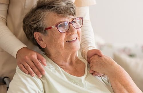 Caregiver gently holding the hand of a seated senior resident in a supportive care environment