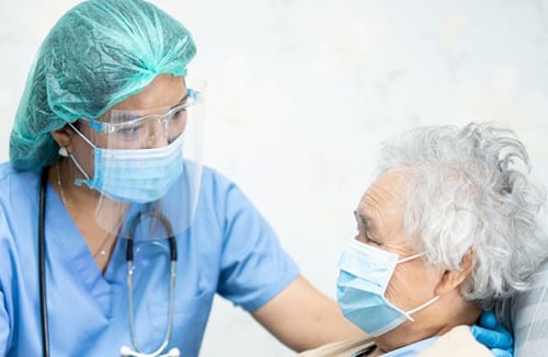 Healthcare professional in protective gear providing support to an elderly resident wearing a face mask.