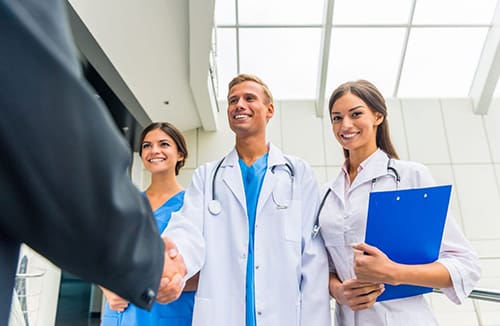 Medical professionals smiling and shaking hands in a bright care environment, fostering community and wellness.