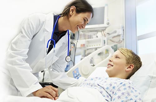 Healthcare professional in a white coat engaging with a young patient in a hospital bed.