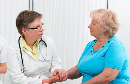Healthcare professional holding hand and talking with a senior woman in a care environment.