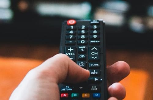 Hand holding and pressing buttons on a television remote control indoors.