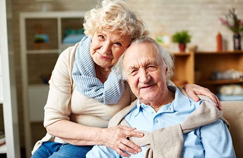 Two older adults sitting together indoors sharing a warm moment of companionship in a senior living community setting.