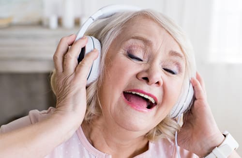 Senior resident listening to music with headphones and singing with eyes closed indoors