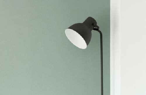 Modern black floor lamp positioned at the corner of a green and white wall.