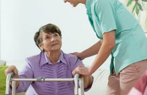 A caregiver assisting a resident using a walker in a senior living community setting.