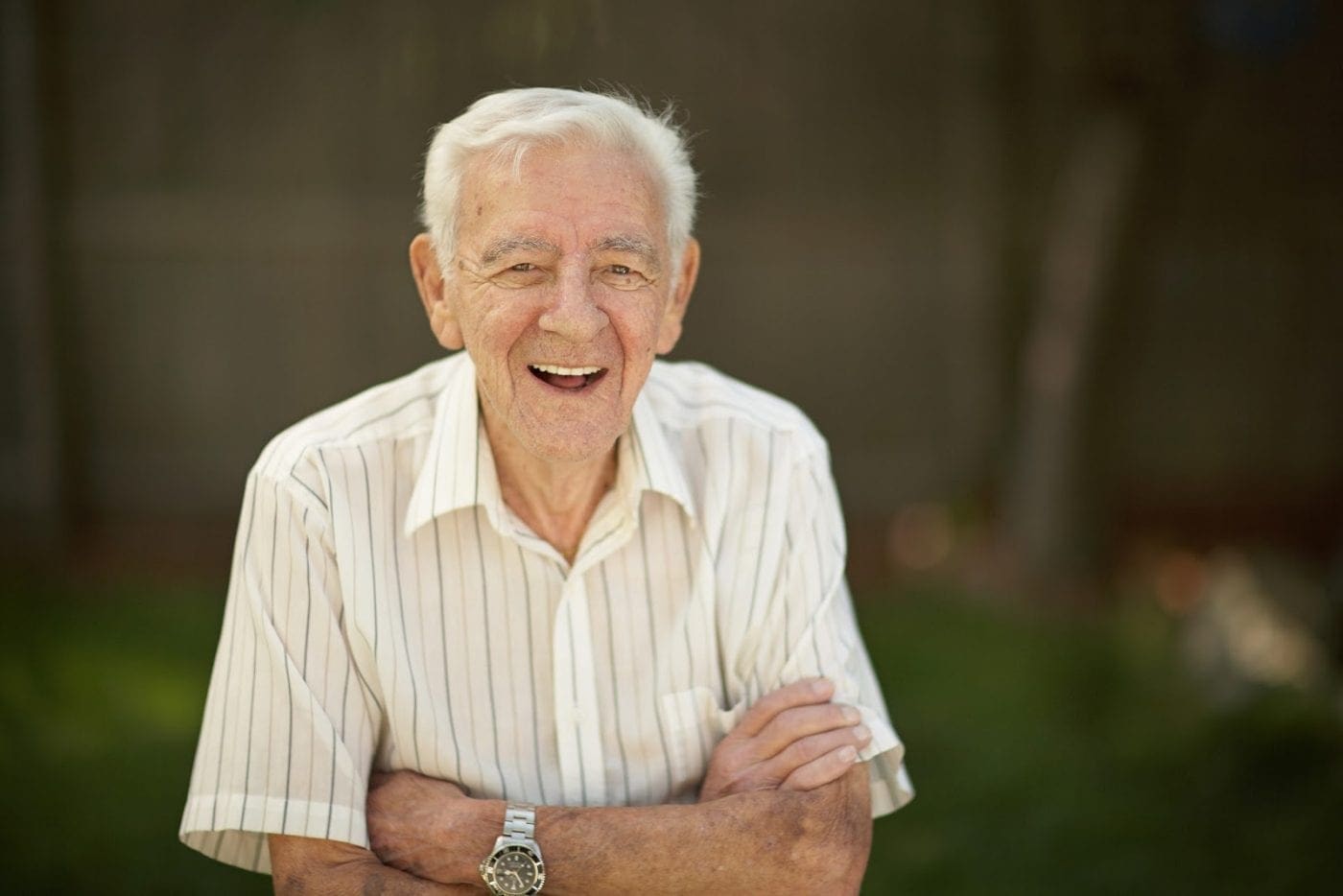 Smiling elderly man standing outdoors with arms crossed in a senior living community setting.