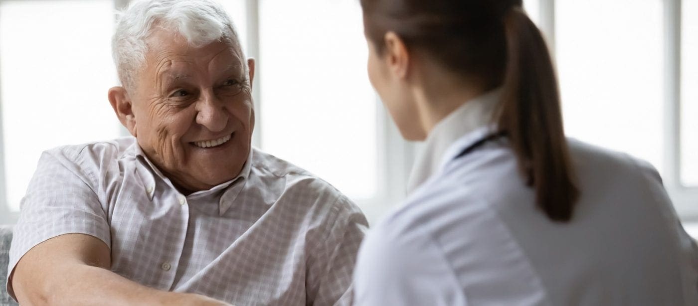 Elderly man smiling while talking with a healthcare professional in a bright room.
