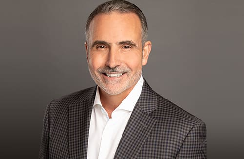 Portrait of a man smiling in a checkered blazer and white shirt against a gray background.