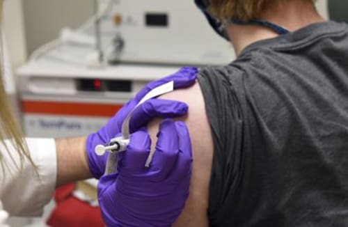 Healthcare professional with gloves giving an injection into a person's upper arm.