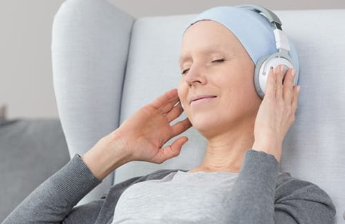 Person with headscarf sitting in a cushioned chair with eyes closed, listening to music on headphones.
