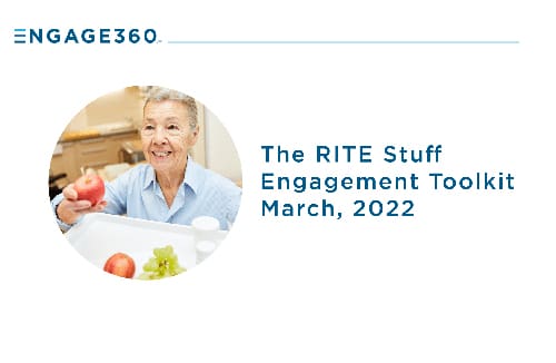 Senior adult smiling while holding an apple at a table with fruit in a senior living setting.