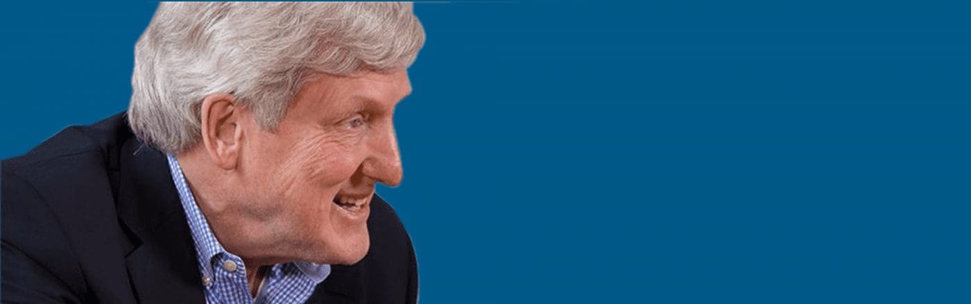 Man smiling and looking sideways against a blue background.