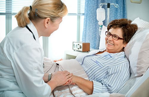 Healthcare professional holding hands with a woman in a hospital bed, sharing a warm and supportive moment in a care environment.