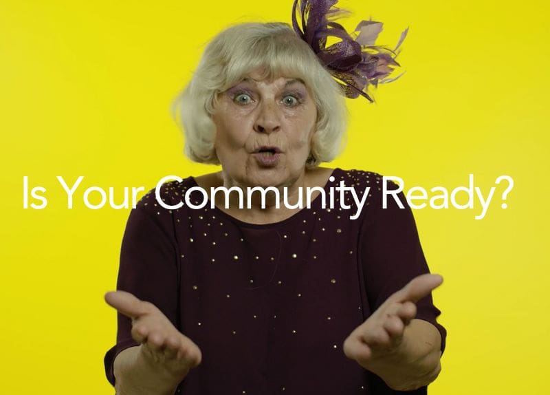 Elderly woman gesturing with hands against a yellow background with text 'Is Your Community Ready?'.