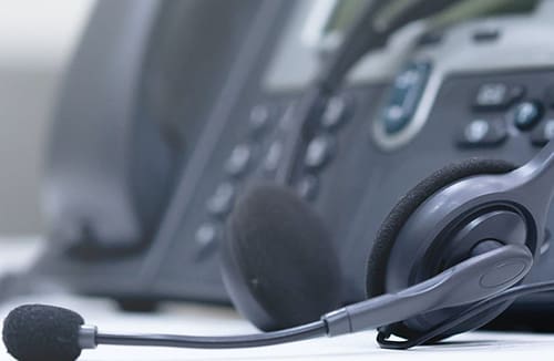Headset with microphone resting near an office telephone on a desk surface.