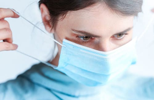 Young woman in scrubs adjusting a medical face mask
