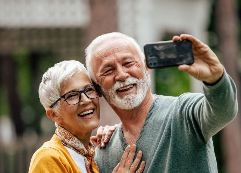 Senior couple smiling and taking a selfie outdoors together, enjoying social engagement.