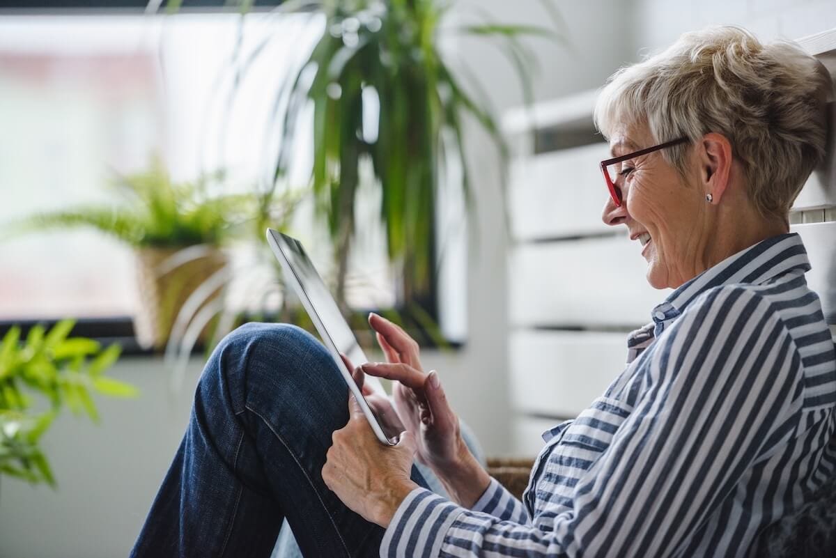 Older woman sitting indoors using a tablet with plants in the background