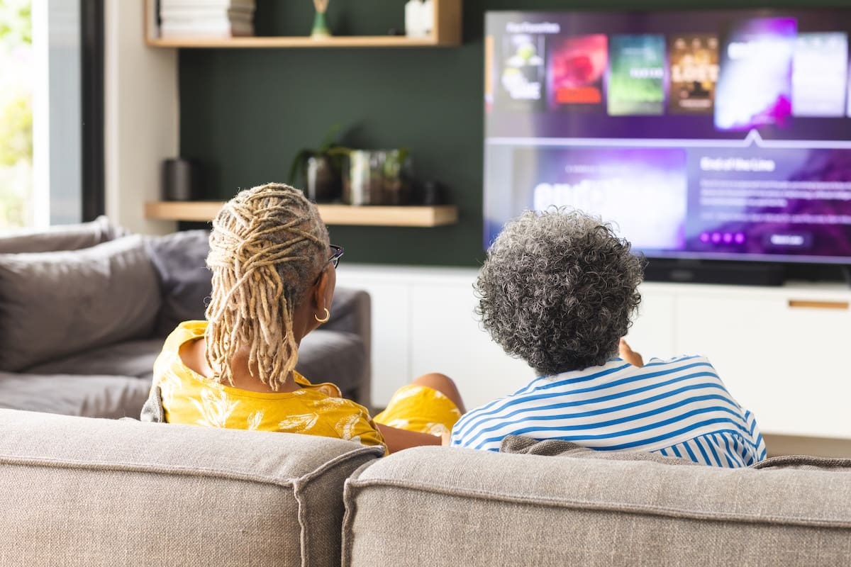 Two people sitting on a couch watching television in a cozy living room setting.