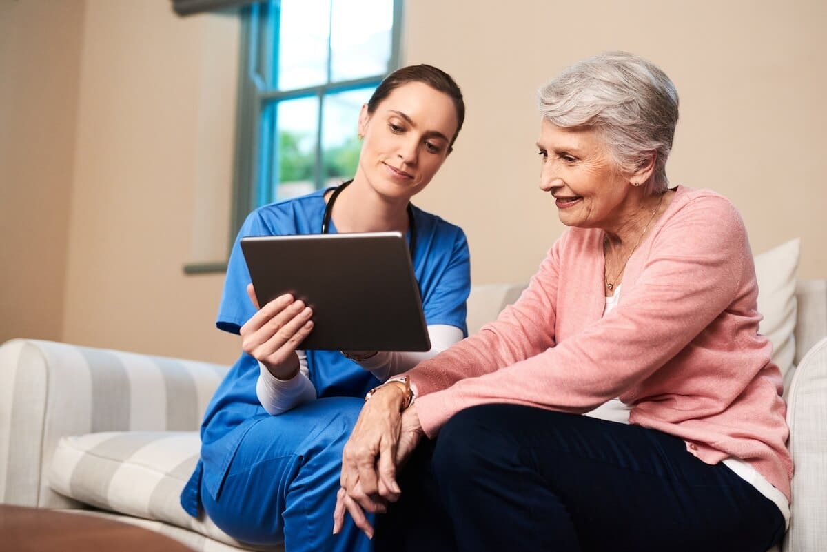 Healthcare professional showing information on a tablet to an older adult in a warm indoor setting.