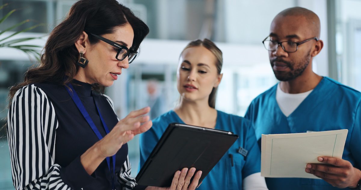 Three professionals engaged in a discussion reviewing information on a tablet and documents in a modern indoor setting.