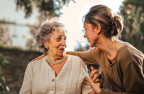 Two women outdoors sharing a warm moment and engaging in a friendly conversation with supportive gesture.
